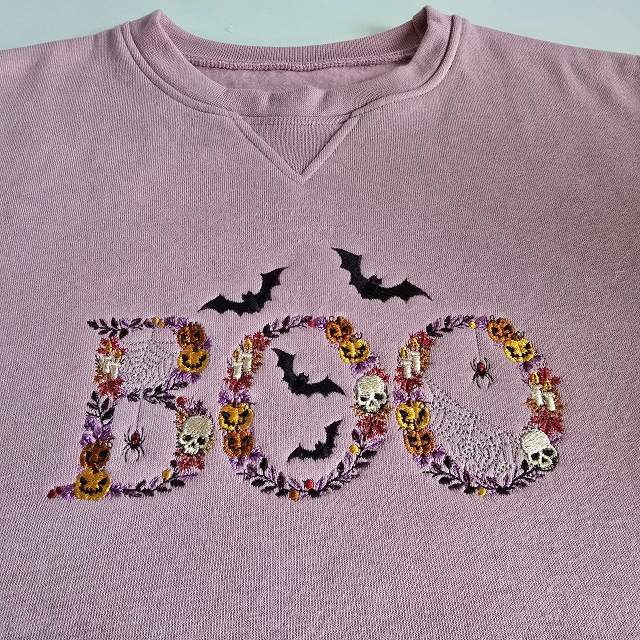 Lilac sweatshirt with detailed “BOO” embroidery featuring bats, skulls, pumpkins, spiders and cobwebs in Halloween colours.