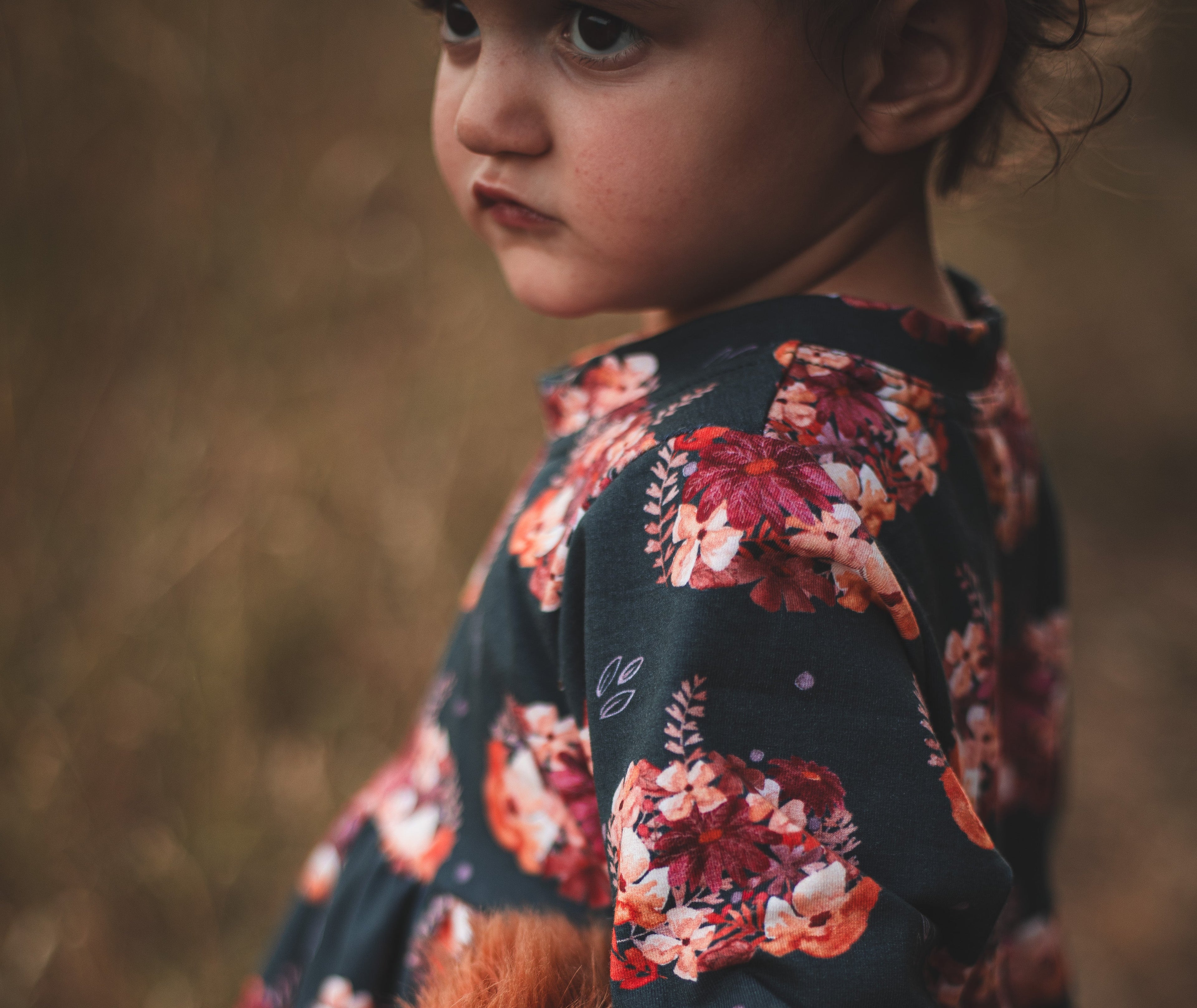 Child wearing a floral dress holding a plush toy in a natural setting