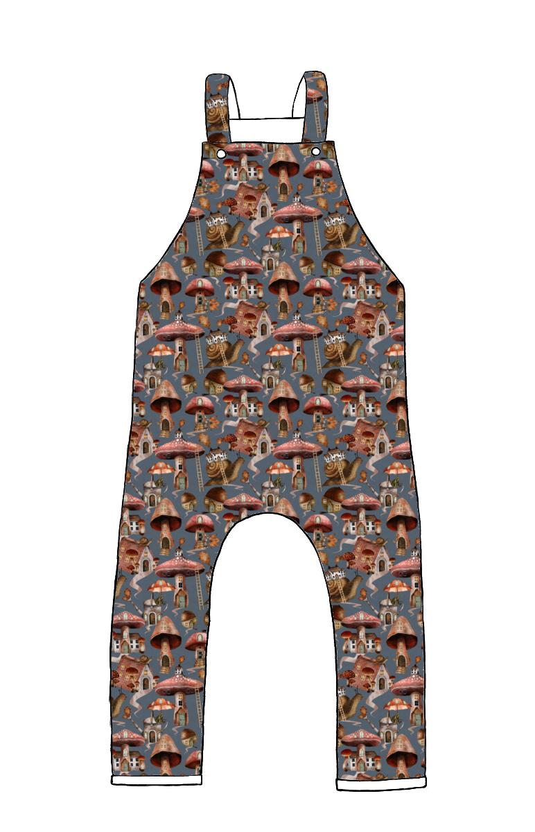 Children’s dungarees in Mushroom Town fabric – blue-grey base with illustrated mushroom houses, snails and forest details.
