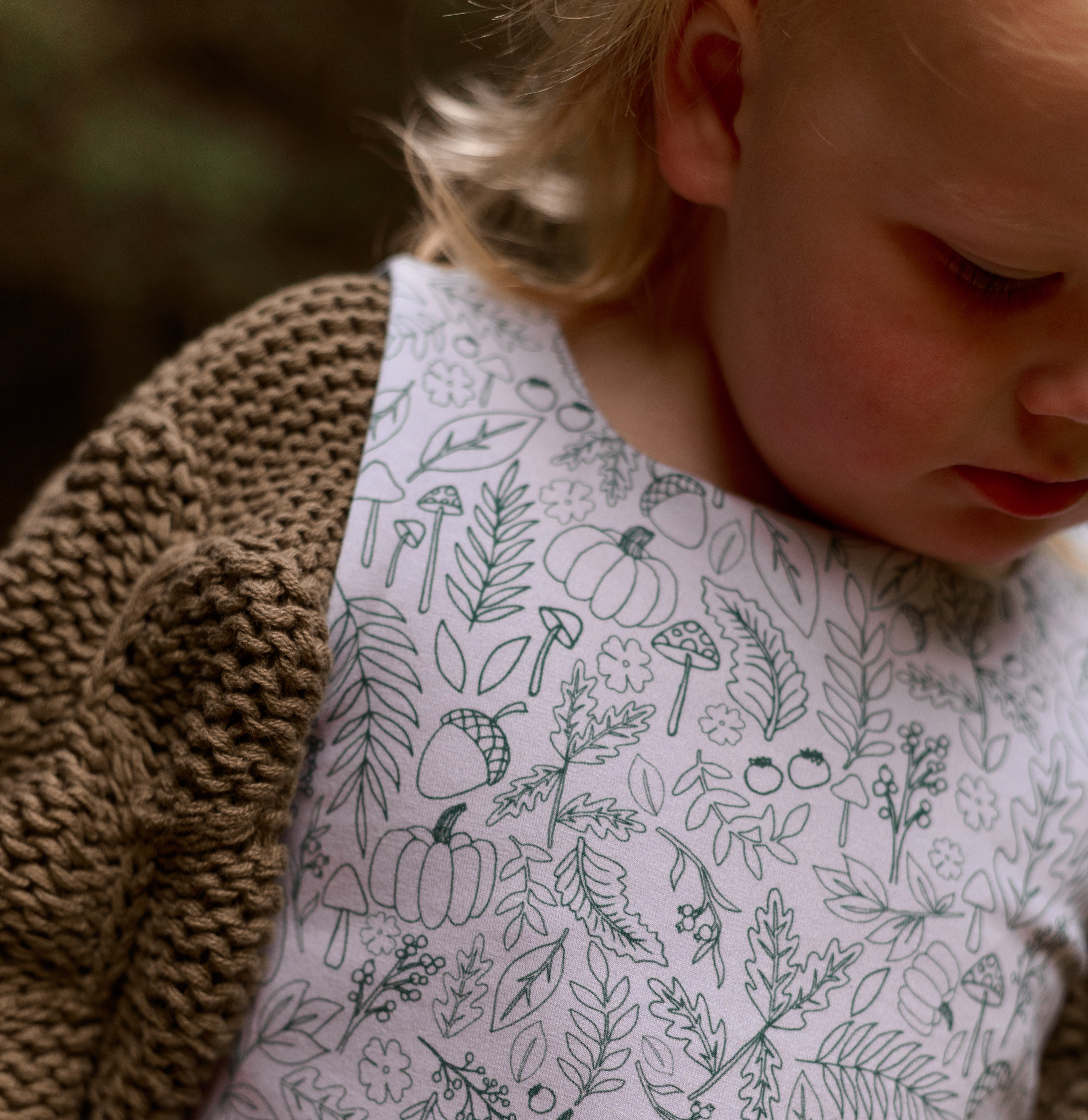 Child wearing a dress with nature-themed pattern, sitting on a textured surface.