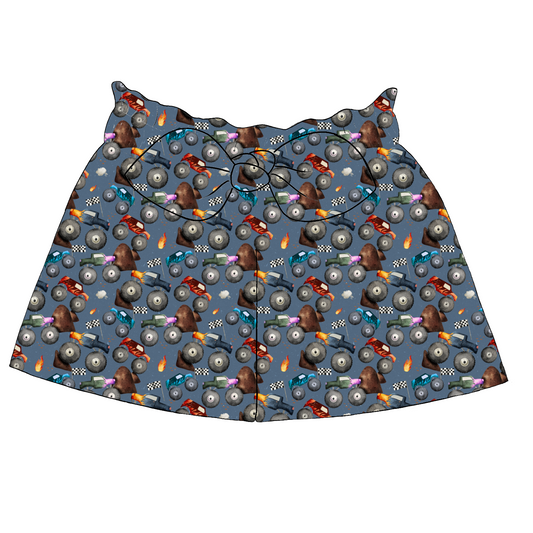 Children’s paperbag shorts in Monster Trucks fabric – denim blue base with monster trucks, racing flags and flames, ruffle waistband and bow.