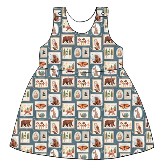 Handmade pinafore dress in Wild Stamps – jersey tile print with woodland creatures, toadstools and folk motifs in dusky blue and rust. Features gathered skirt and popper straps.