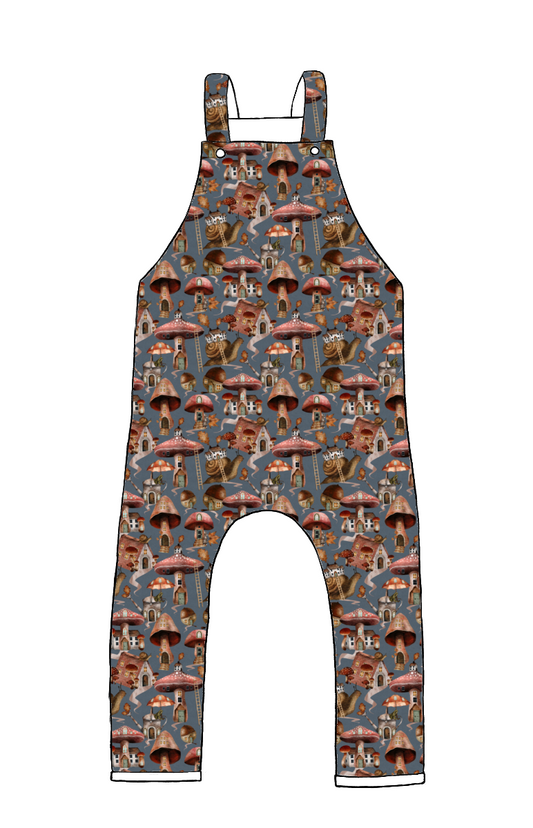 Children’s dungarees in Mushroom Town fabric – blue-grey base with illustrated mushroom houses, snails and forest details.