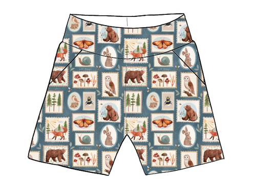 Children’s pocket shorts in Wild Stamps fabric – blue-grey base with animal portraits, mushrooms and insects in illustrated postage stamp frames.