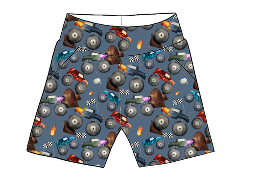 Children’s pocket shorts in Monster Trucks fabric – blue base with colourful monster trucks, flames, ramps and racing flags.