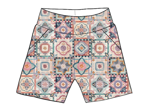 Children’s handmade pocket shorts in Faro fabric – a repeating tile pattern in blush, mustard, teal and terracotta on a soft white base.