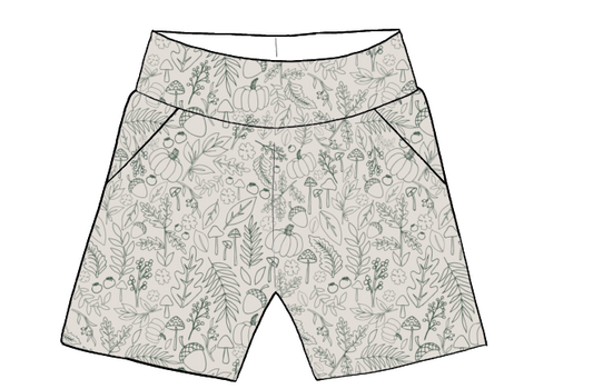 Children’s pocket shorts in cream fabric with sage green autumn-themed line drawings of leaves and pumpkins.
